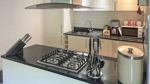 Een moderne keuken met een gasfornuis, een spoelbak, een magnetron en een waterkoker.