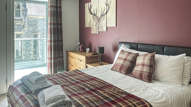 Een slaapkamer met een bed, een houten nachtkastje, een spiegel en een raam met gordijnen.