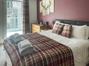 A bedroom with a bed, a wooden nightstand, a mirror, and a window with curtains. - Raven Wing 17 - UKC4882 (Fort Augustus)