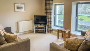 A living room with two sofas, a TV stand, and a window with a view of a garden. - Raven Wing 11 - Kintail Apartment - UKC4883 (Fort Augustus)