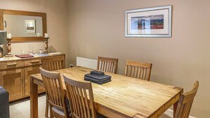 A dining area with a wooden table and chairs, a mirror, and a framed picture on the wall. - Raven Wing 11 - Kintail Apartment - UKC4883 (Fort Augustus)