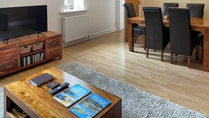 A modern living room with a TV, wooden entertainment unit, dining table with chairs, and a fireplace. - Moat House 6 - UKC4889 (Fort Augustus)