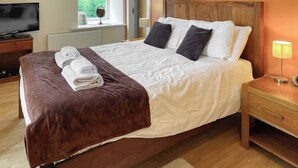 A neatly made bed with a brown and white duvet, a bedside lamp, and a TV on a wooden stand. - Moat House 6 - UKC4889 (Fort Augustus)