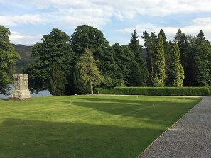 Une pelouse bien entretenue, agrémentée d’un monument en pierre, de haies taillées avec soin et de grands arbres en arrière-plan.