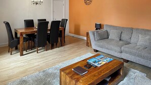 A living room with a wooden dining table, black chairs, a grey sofa, and a coffee table with books. - Moat House 6 - UKC4889 (Fort Augustus)