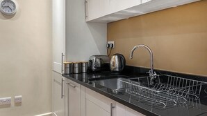 A kitchen with white cabinets, a black countertop, a stainless steel sink, a kettle, a toaster, and a clock on the wall. - Moat House 6 - UKC4889 (Fort Augustus)