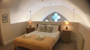 A bedroom with a large bed, two bedside tables, a window with a flower design, and a ceiling light. - Old School 14 - UKC4893 (Fort Augustus)