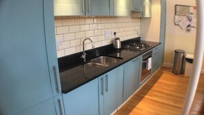 A modern kitchen with light blue cabinets, a black countertop, stainless steel sink, and a gas stove. - Old School 14 - UKC4893 (Fort Augustus)