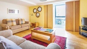 Een woonkamer met een bank, een bijzettafeltje en uitzicht op een gebouw door een groot raam.