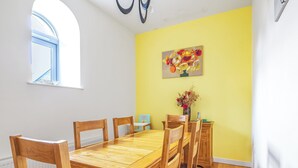 Een eethoek met een houten tafel en stoelen, een vaas met gedroogde bloemen en een schilderij aan de muur.