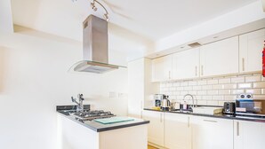 Een moderne keuken met witte kastjes, een roestvrijstalen afzuigkap, een gasfornuis en een koffiezetapparaat.