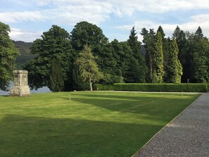 A well-maintained golf course with a stone monument, neatly trimmed hedges, and a variety of trees in the background. - Abbey Garden - UKC4894 (Fort Augustus)