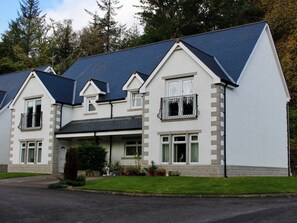 A two-story house with a steeply pitched roof, a front porch, and a small front yard with potted plants. - 2 bedroom accommodation in Invergarry (Invergarry)