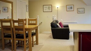 A dining area with wooden chairs and a table, a black sofa with cushions, and a floor lamp. - 2 bedroom accommodation in Invergarry (Invergarry)