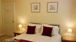 A neatly made bed with a red and white patterned bedspread, two red pillows, and two bedside lamps. - 2 bedroom accommodation in Invergarry (Invergarry)