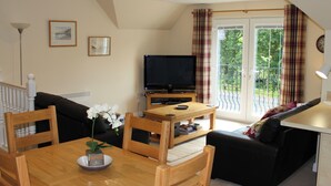 A cozy living room with a dining table, chairs, a sofa, a TV, and a balcony with curtains. - 2 bedroom accommodation in Invergarry (Invergarry)