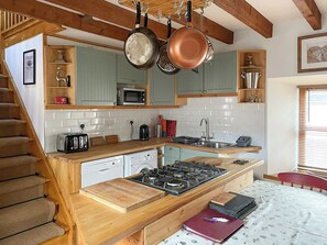 A kitchen with a wooden countertop, a gas stove, a microwave, and hanging pots. - 2 bedroom accommodation in Fort Augustus (Fort Augustus)