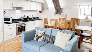 A modern kitchen with white cabinets, a dining area with wooden chairs, and a blue sofa with decorative pillows. - Monastery 17 - UKC4888 (Fort Augustus)