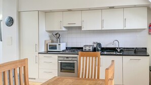 A modern kitchen with white cabinets, a wooden dining table, and basic appliances like a microwave, toaster, and oven. - Monastery 17 - UKC4888 (Fort Augustus)