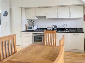 Eine moderne Küche mit weißen Schränken, einem Holztisch und üblichen Geräten wie Mikrowelle, Toaster und Backofen.