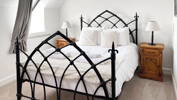 A bed with a black wrought iron frame, white bedding, and two bedside tables with lamps. - Monastery 17 - UKC4888 (Fort Augustus)