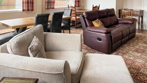 Un salon chaleureux avec un canapé en cuir, un fauteuil à motifs et un coin repas comprenant une table et des chaises en bois.