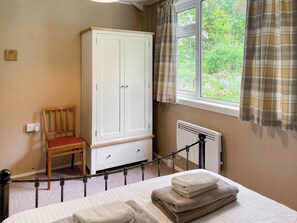 A bedroom with a bed, a wooden chair, a white wardrobe, a window with curtains, and a radiator.
