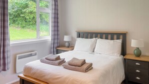 Un lit bien fait, avec deux serviettes pliées, une table de chevet avec une lampe et une fenêtre avec des rideaux.