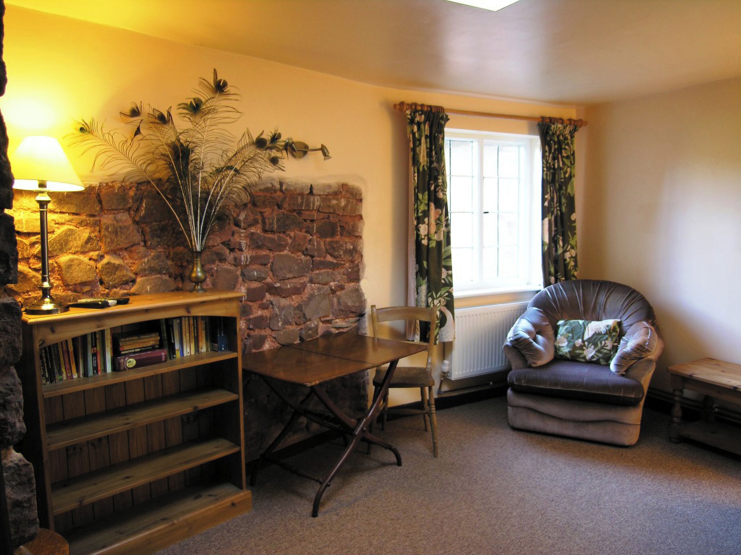 Un salon chaleureux avec un mur en pierre, une bibliothèque en bois, un fauteuil en cuir et une table avec une chaise.