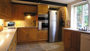 Une cuisine dotée de meubles en bois, d’un réfrigérateur en acier inoxydable, d’un four à micro-ondes et d’un mur décoratif en pierre.
