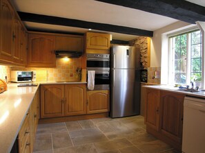 A kitchen with wooden cabinets, a stainless steel refrigerator, a microwave, and a stone accent wall. - 6 bedroom accommodation in Timberscombe, near Minehead (Timberscombe, near Minehead)
