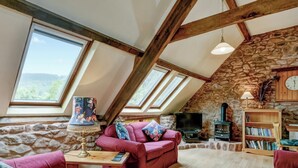 Un appartement-loft chaleureux avec un mur en pierre, des poutres en bois, un canapé rouge, un téléviseur et une bibliothèque.