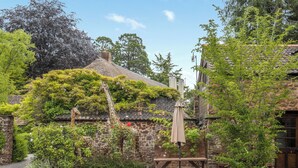 Un espace extérieur rustique agrémenté d’un banc en bois, d’une pergola et d’un bâtiment en briques recouvert de lierre.