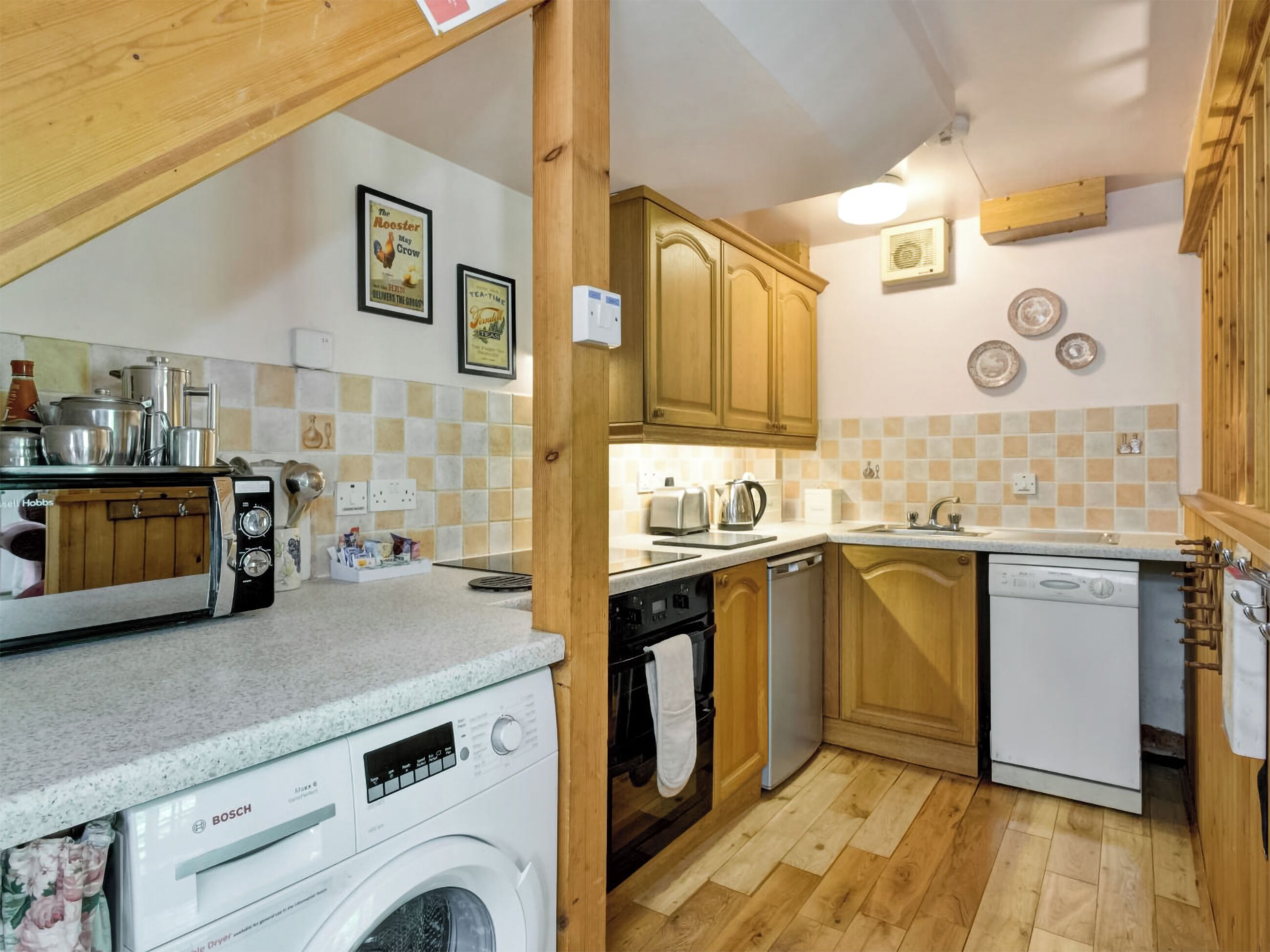 A compact kitchen with a Bosch washing machine, a microwave, a toaster, and wooden cabinets.