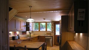 Uma cozinha compacta com armários de madeira, uma ilha central com cadeiras, um lustre pendente e uma janela que oferece iluminação natural.