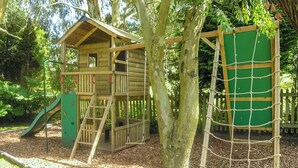 A wooden play structure with a slide and climbing net, surrounded by trees and mulch. - 2 bedroom accommodation in Timberscombe, near Minehead (Timberscombe, near Minehead)