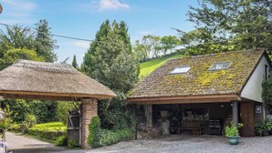 A rustic building with a thatched roof structure, a covered porch, and a gravel driveway. - 2 bedroom accommodation in Timberscombe, near Minehead (Timberscombe, near Minehead)