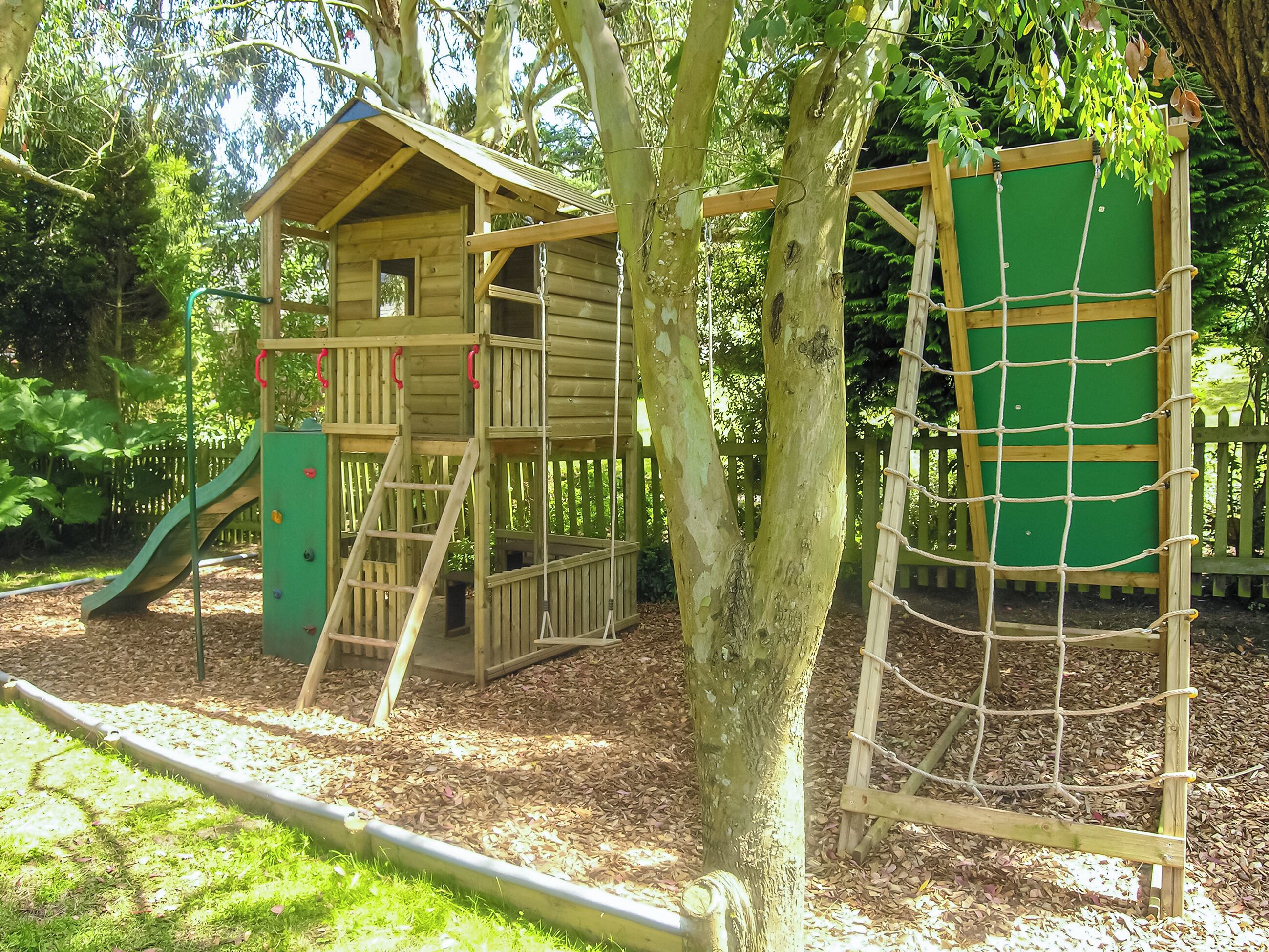 Una estructura de madera para juegos con un tobogán, una red de escalada y una casita.