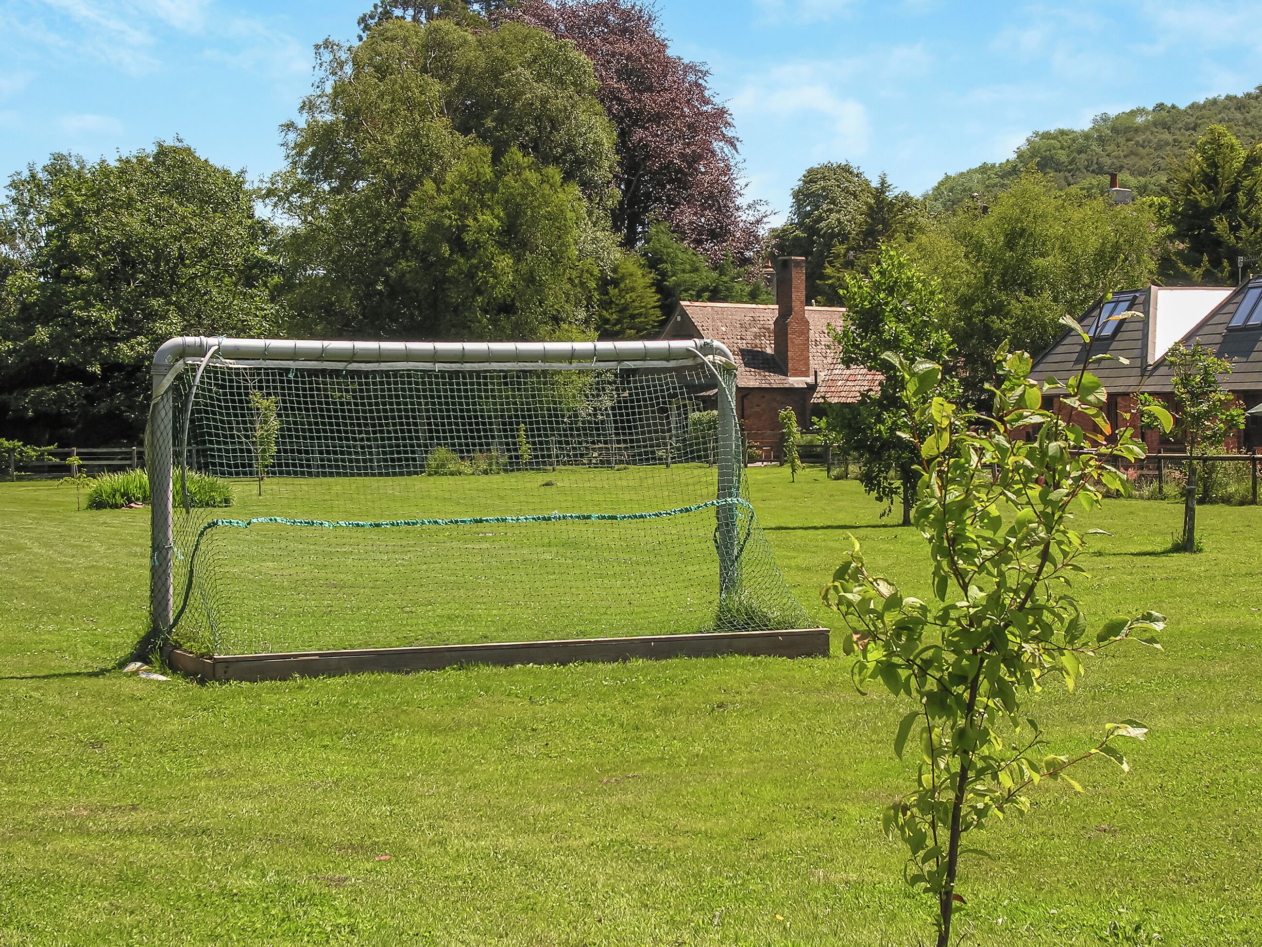 A soccer goal in a grassy field with a brick building in the background.