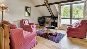 A cozy living room with wooden beams, a fireplace, a television, and two red sofas. - 2 bedroom accommodation in Timberscombe, near Minehead (Timberscombe, near Minehead)