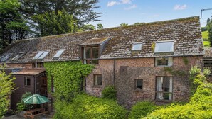 A stone building with ivy-covered walls, a gravel driveway, and a wooden bench. - 2 bedroom accommodation in Timberscombe, near Minehead (Timberscombe, near Minehead)