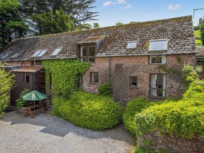 A stone building with ivy-covered walls, a gravel driveway, and a wooden bench. - 2 bedroom accommodation in Timberscombe, near Minehead (Timberscombe, near Minehead)