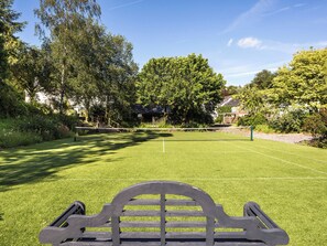 A tennis court with a wooden bench in the foreground, surrounded by lush greenery and trees. - 1 bedroom accommodation in West Anstey (West Anstey)