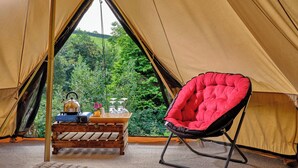 Una carpa con una mesa de madera y una silla roja, una tetera y una bandeja con vasos.