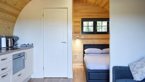 Een compacte slaapkamer met een bed, een klein nachtkastje en een raam. Grenzend hieraan een kitchenette met een fornuis, een spoelbak en kastjes.