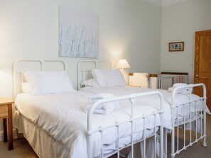 Een tweepersoonsbed met metalen frame, een nachtkastje, een lamp, een houten deur en een schilderij aan de muur.
