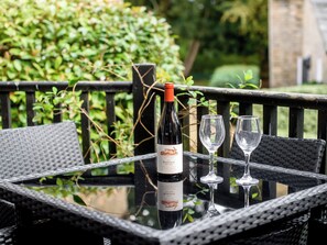 Een fles wijn en twee glaasjes op een glazen tafel buiten.