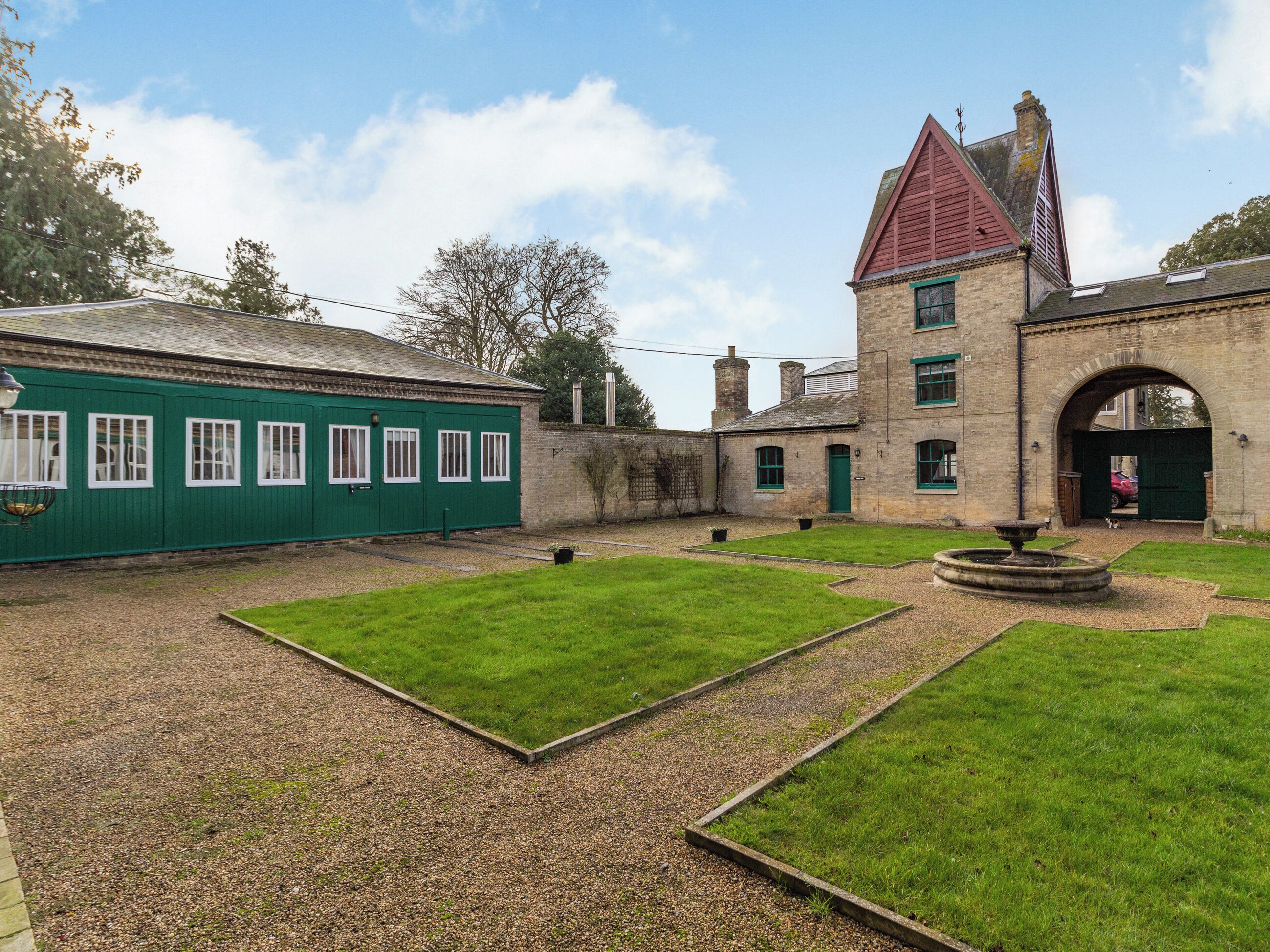 A courtyard with a green lawn, a fountain, and a building with a red roof and stone walls.