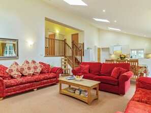 A spacious living room with two red sofas, a wooden coffee table, and a staircase leading to an upper floor. - 3 bedroom accommodation in Bury St. Edmunds (Bury St. Edmunds)