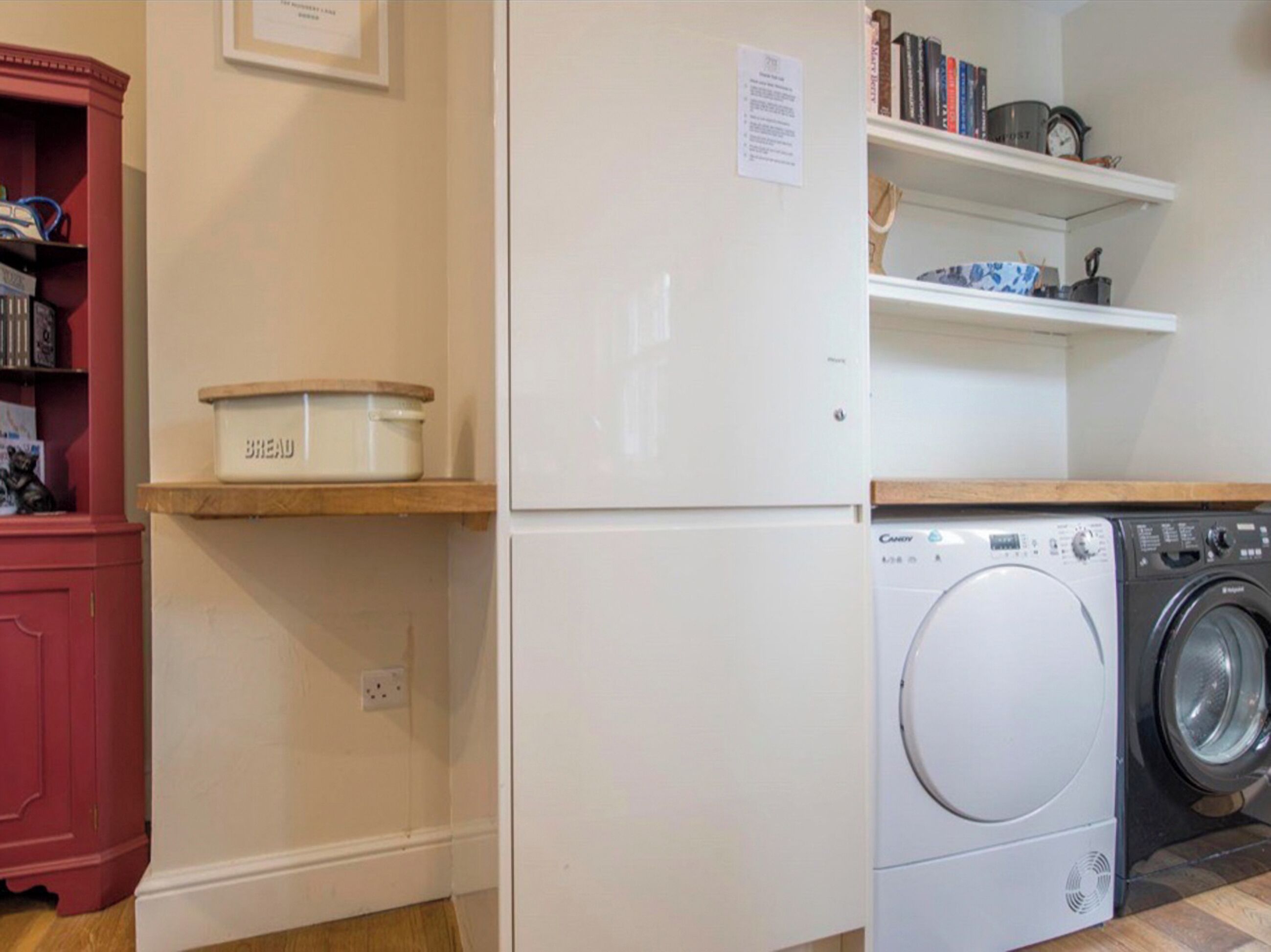 Une cuisine compacte avec un réfrigérateur blanc, un lave-linge et un récipient à pain placé sur une étagère.